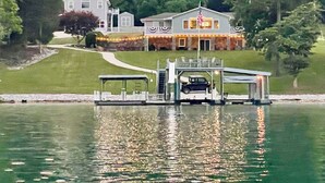 Une grande maison avec un quai et un bateau, entourée d’arbres et bordée par un lac.