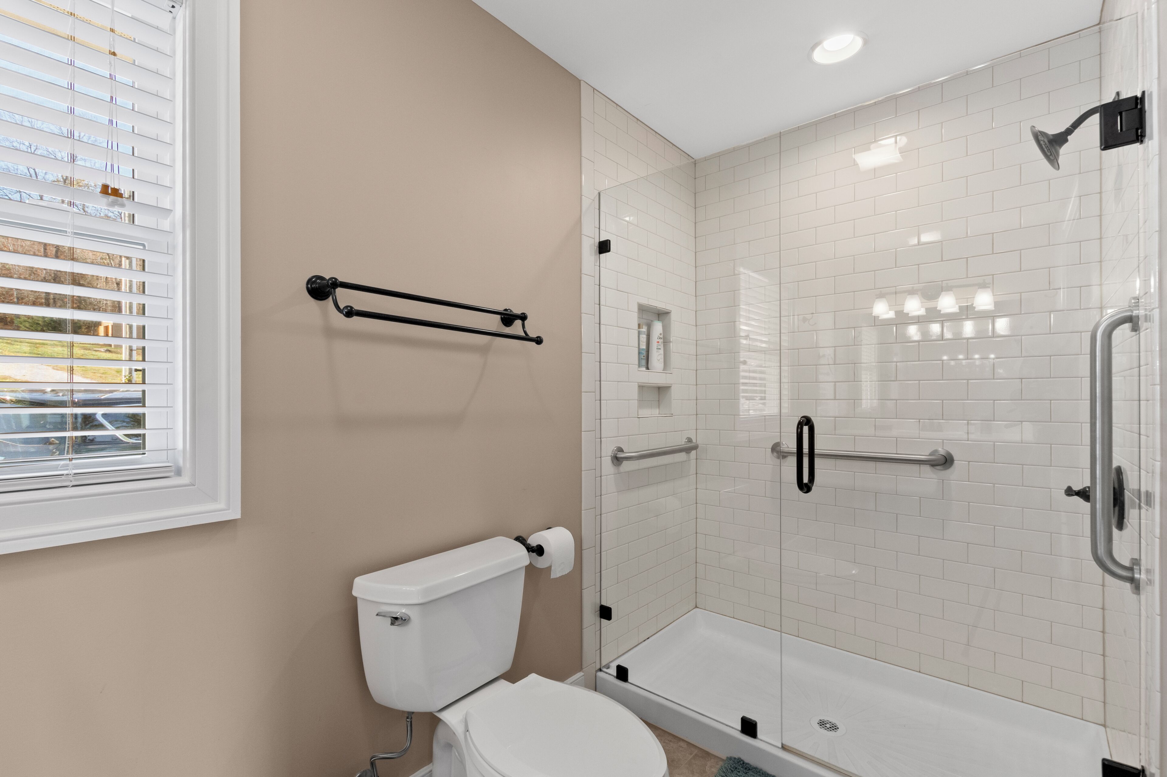 A bathroom with a toilet, a glass-enclosed shower, and a window with blinds.