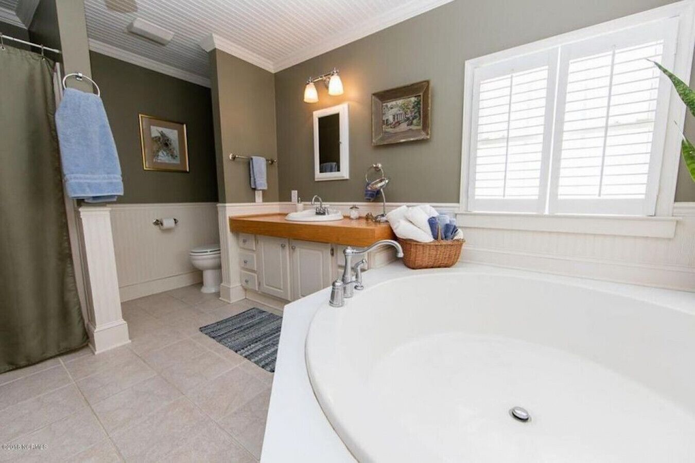 A bathroom with a large bathtub, a vanity with a sink, a mirror, and a window with blinds.