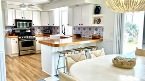 Eine moderne Küche mit weißen Schränken, einer zentralen Kochinsel mit Barhocker, einem eingebauten Backofen und einem Essbereich mit rundem Tisch.