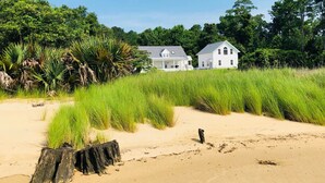 Ein Strandgrundstück mit einem großen weißen Haus, Sandstrand und dichter grüner Vegetation.