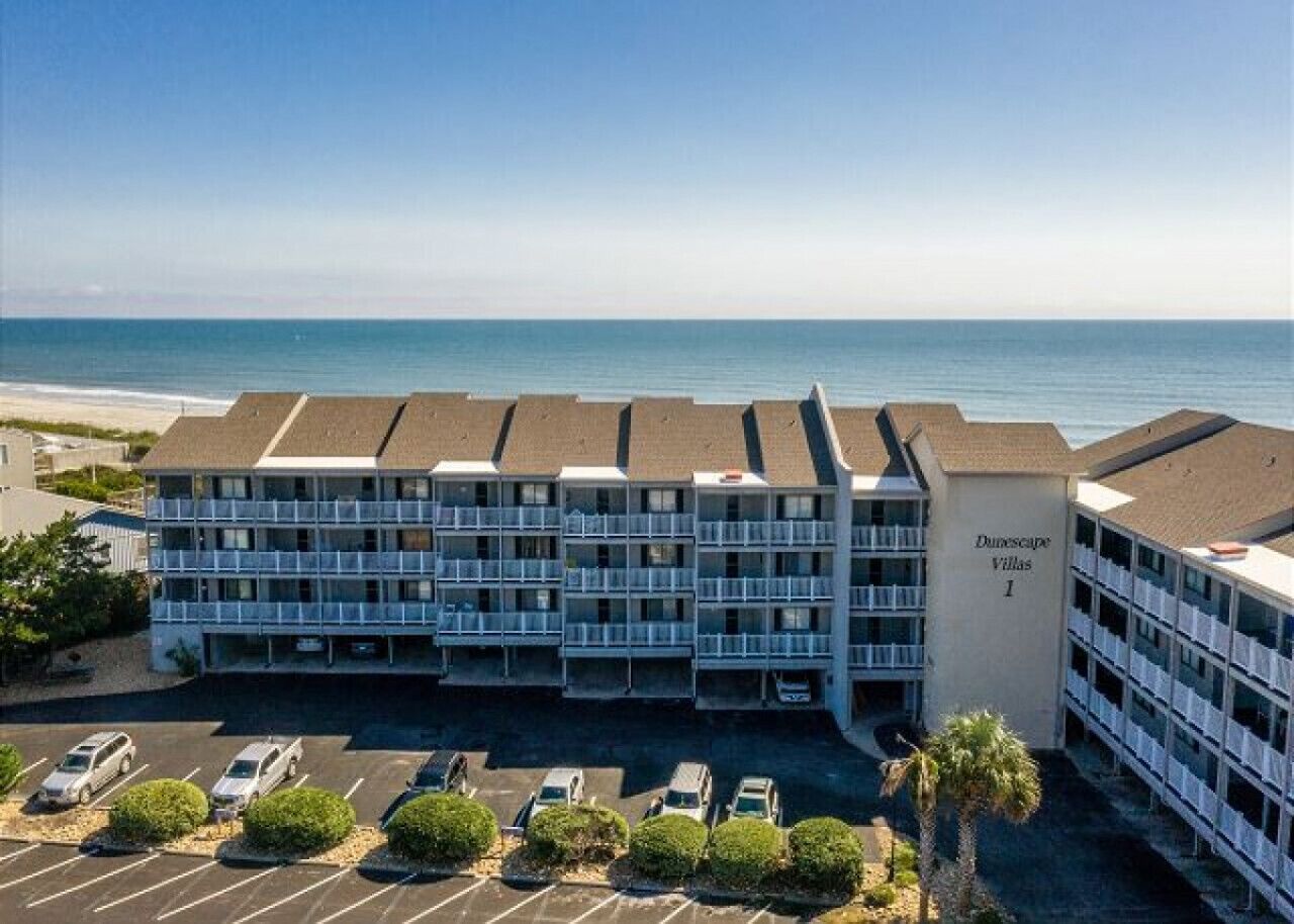 A multi-story building with balconies, a parking lot, and a view of the ocean.