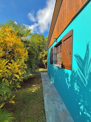 Un edificio con rivestimento in legno e una parete blu, un vialetto in piastrelle e vegetazione tropicale.