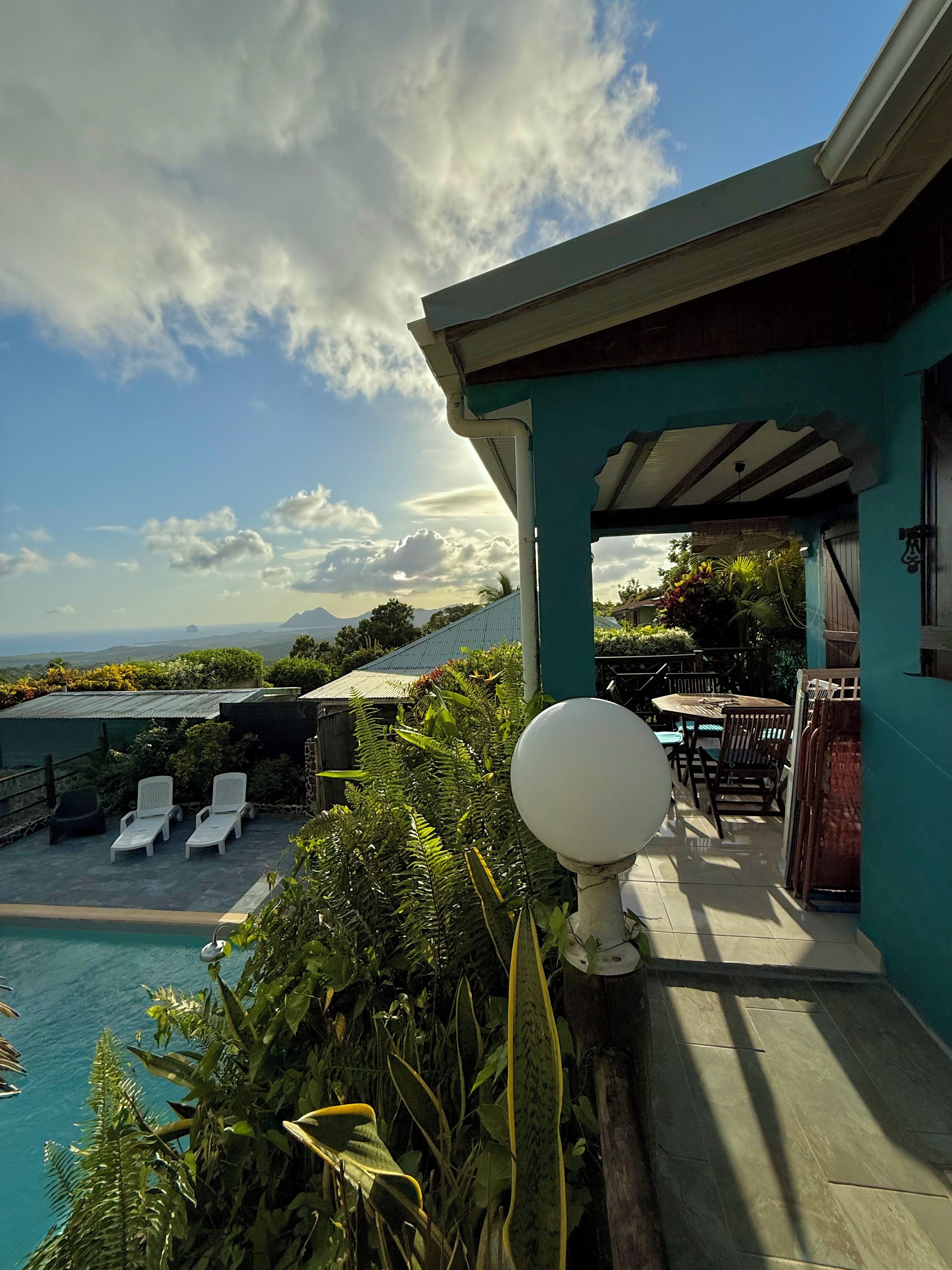 A poolside area with lounge chairs, a table, and a view of the ocean and mountains.