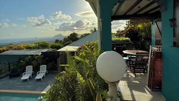 A poolside area with lounge chairs, a table, and a view of the ocean and mountains.