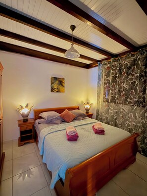 A bedroom with a wooden bed, two bedside lamps, a ceiling fan, and a floral curtain.
