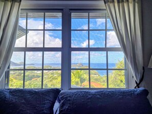 A room with a large window, two beds with blue bedding, and a view of a landscape with greenery and a body of water. - Panoramic Views as Sunsets await, Close to Beaches, Sandals Golf and Cabot Golf (Cap Estates)