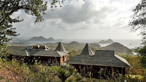 A view of a coastal area with two buildings with pointed roofs, surrounded by vegetation and overlooking the sea. - Panoramic Views as Sunsets await, Close to Beaches, Sandals Golf and Cabot Golf (Cap Estates)