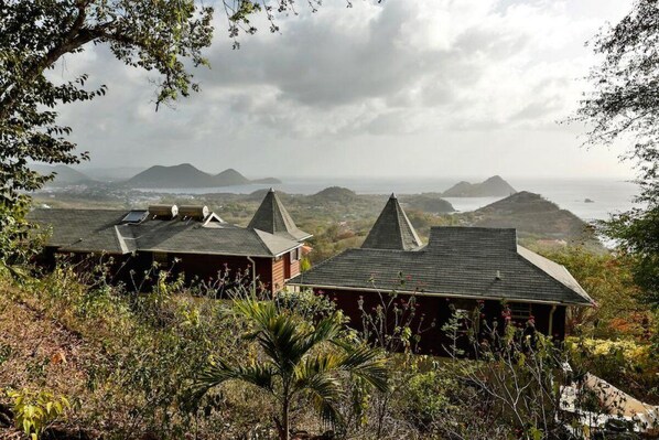 A view of a coastal area with two buildings with pointed roofs, surrounded by vegetation and overlooking the sea. - Panoramic Views as Sunsets await, Close to Beaches, Sandals Golf and Cabot Golf (Cap Estates)