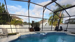 A swimming pool with a tiled edge, a covered area with chairs, and a fenced backyard.