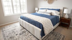 A bedroom with a large bed, two bedside tables with lamps, a window, and decorative wall art.