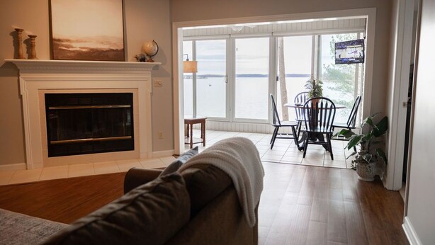 A living room with a fireplace, a sofa, a dining area with chairs, and a view of the water outside.