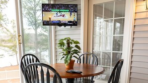A dining area with a round table, four chairs, a potted plant, and a television mounted on the wall.