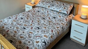 Un llit ben arrenjat amb un edredó estampat amb motius florals, dues taules de nit amb làmpades, un mirall rodó i un quadre al mur.