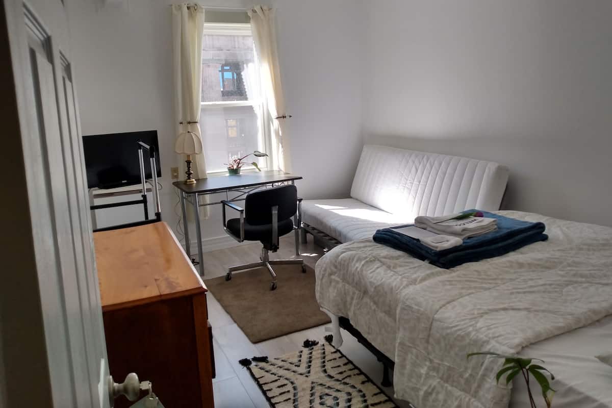 Ein Schlafzimmer mit Bett, Schreibtisch, Stuhl und einem Fenster mit Vorhängen.
