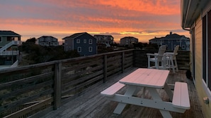 A wooden deck with picnic tables overlooking a residential area during sunset. - Water Music OBX:  Ocean views, easy beach access, private pool.  Pet friendly. (Corolla)
