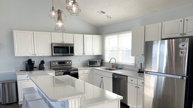 A modern kitchen with white cabinets, stainless steel appliances, and a central island. - Water Music OBX:  Ocean views, easy beach access, private pool.  Pet friendly. (Corolla)