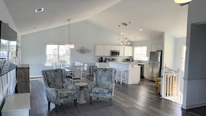 A spacious living area with a round rug, two patterned sofas, a dining table, and a kitchen in the background. - Water Music OBX:  Ocean views, easy beach access, private pool.  Pet friendly. (Corolla)