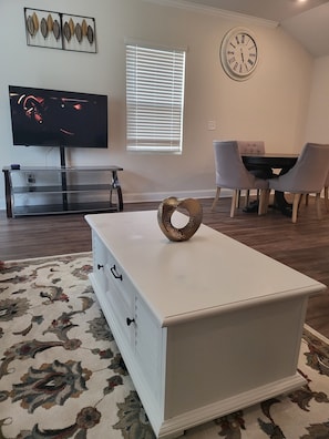 A living room with a white entertainment center, a flat-screen TV, a dining area with a table and chairs, and a wall clock. - Cheerful home entire 3 bedroom with massage chair 
 (Raleigh)
