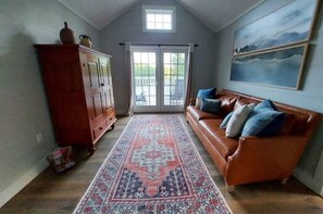 A living room with a brown leather sofa, a patterned rug, a wooden cabinet, and a large window with a view.