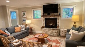 Una sala de estar acogedora con chimenea, dos sofás, sillas de mimbre y una mesa de centro.