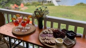 Una mesa de madera con vistas a un lago y un bosque, con una tabla de embutidos y copas de vino tinto.