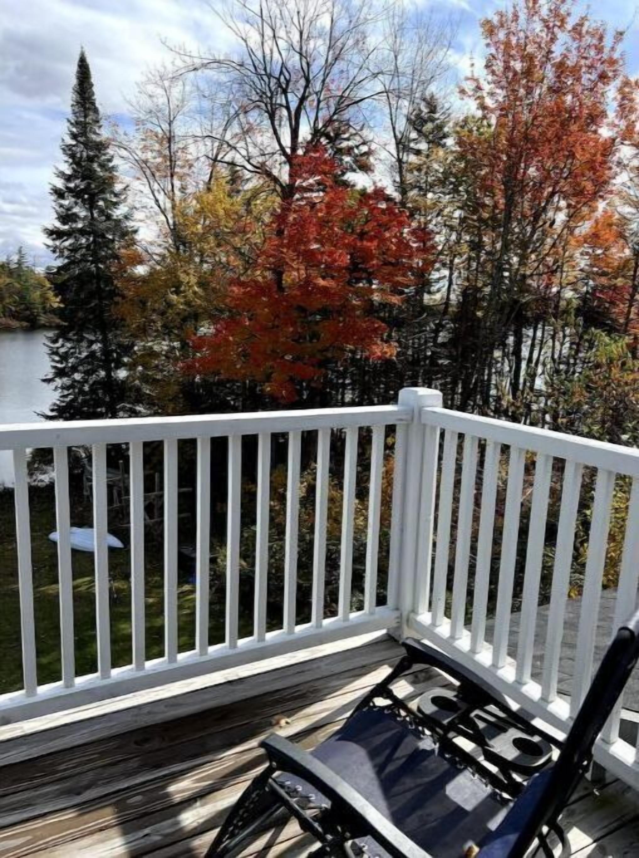 Une terrasse en bois avec une balustrade blanche, un barbecue noir et une chaise.