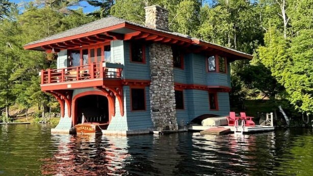 Una casa flotante con chimenea de piedra, un balcón y un muelle.
