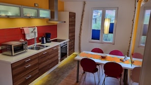 Cocina funcional con microondas, cafetera y horno. Cuenta con una mesa de comedor con sillas y una ventana con persianas.
