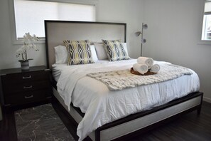 A modern bedroom with a large bed, two bedside tables, a nightstand, a decorative plant, and a floor lamp. - Bloomfield Hills Modern, Luxurious Ranch, 1900 Sq Ft, 3 Bedroom/2.5 Bath + Patio (Bloomfield Hills)