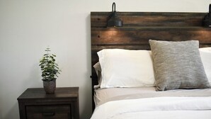 Une chambre à coucher avec une tête de lit en bois, une table de chevet ornée d’une plante et une lampe.