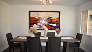 Une salle à manger avec une table rectangulaire, six chaises et un grand tableau abstrait accroché au mur.