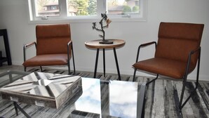 Une pièce comprenant deux fauteuils en cuir marron, une petite table ronde en bois et une table basse en verre ornée d’un motif géométrique.