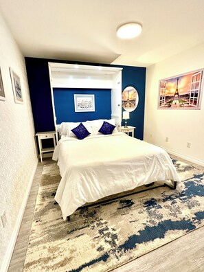 Une chambre à coucher avec un lit, une table de chevet, une lampe fixée au mur et une image de la Tour Eiffel.