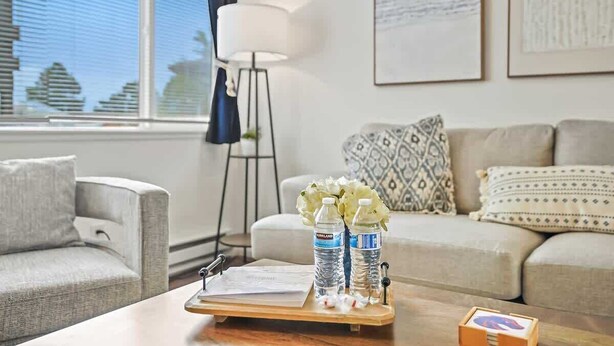 A living room with a sofa, a coffee table with a tray holding water bottles and a flower vase, a floor lamp, and framed artwork on the wall. - Single Level Homestay - Prime Location (Boise)