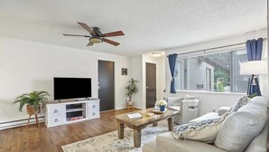 A living room with a flat-screen TV, wooden coffee table, sofa, and a ceiling fan. - Single Level Homestay - Prime Location (Boise)