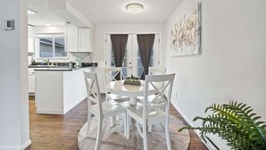 A modern kitchen with white cabinets, a central island, and a dining area with a round table and white chairs. - Single Level Homestay - Prime Location (Boise)