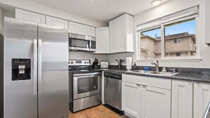 A modern kitchen with stainless steel appliances, white cabinetry, and a window providing a view of the neighborhood. - Single Level Homestay - Prime Location (Boise)