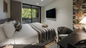 Una habitación de hotel con una cama grande, un escritorio, una silla, un televisor y una ventana con vistas a árboles.