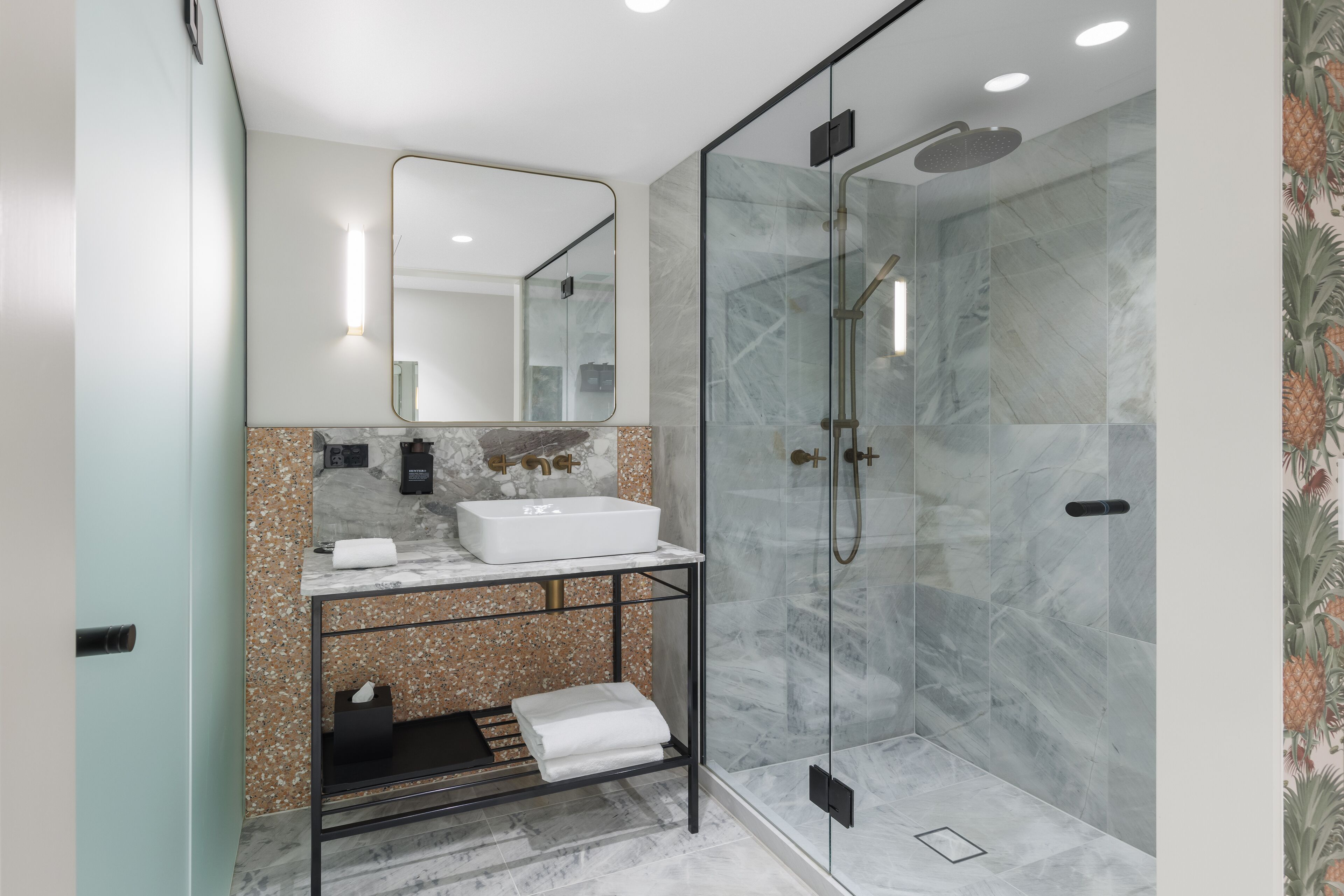 Un baño moderno con ducha de vidrio, lavamanos blanco y encimera de mármol.