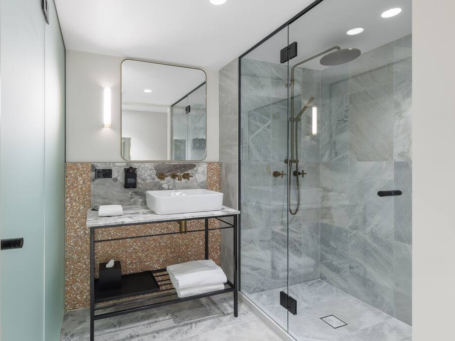 Un baño moderno con ducha de vidrio, lavamanos blanco y encimera de mármol.
