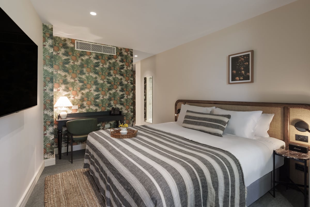 A hotel room with a bed, a desk, a chair, a lamp, and a framed picture on the wall.