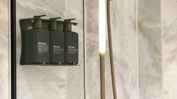 A bathroom with a marble wall, a shower with a handheld showerhead, and three black bottles of Hunter® shampoo.