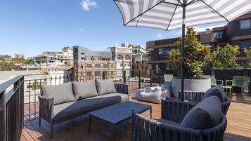 A rooftop terrace with outdoor furniture, a large umbrella, and a view of surrounding buildings.