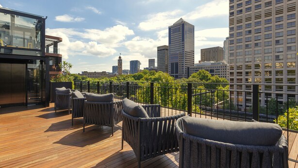Terraza en la azotea con mobiliario de mimbre y vistas a un horizonte urbano.