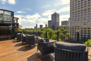 Terraza en la azotea con mobiliario de mimbre y vistas a un horizonte urbano.
