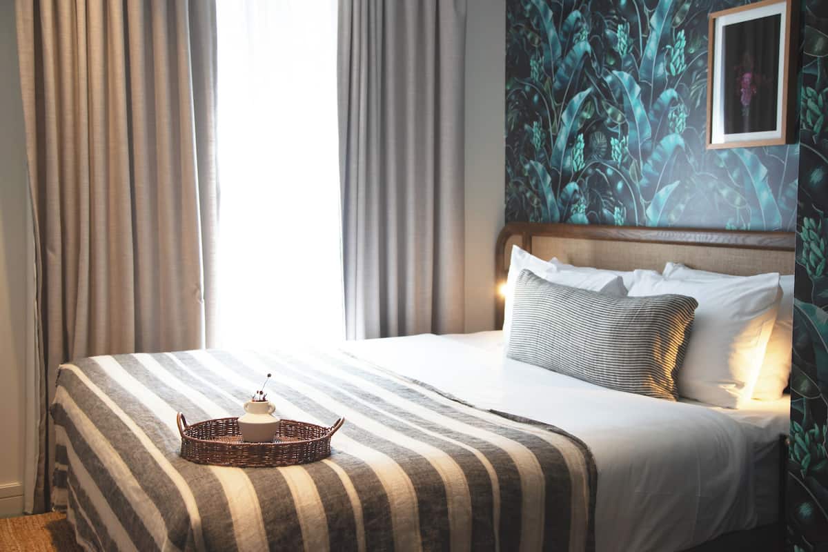 A neatly made bed with striped bedding, a small wicker tray with a teapot, and a framed picture on the wall.