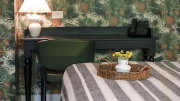 Una habitación con una colcha a rayas, una cesta de mimbre con flores amarillas, un jarrón blanco, una lámpara, un teléfono y una silla.