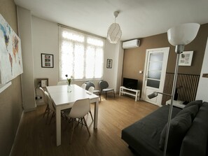 A modern living room with a white table, grey sofa, and a TV on a stand.