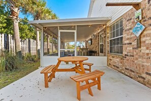 Een overdekt terras met een houten tafel en banken, bakstenen muren en uitzicht op de achtertuin.